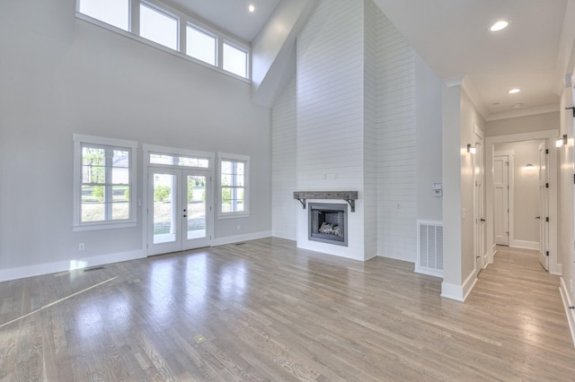 unfurnished living room featuring french doors, light hardwood / wood-style floors, a high ceiling, and ornamental molding