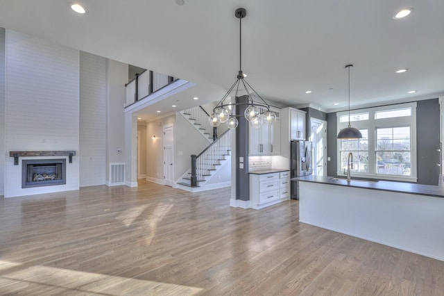 kitchen featuring sink, hanging light fixtures, stainless steel fridge with ice dispenser, light hardwood / wood-style flooring, and white cabinets