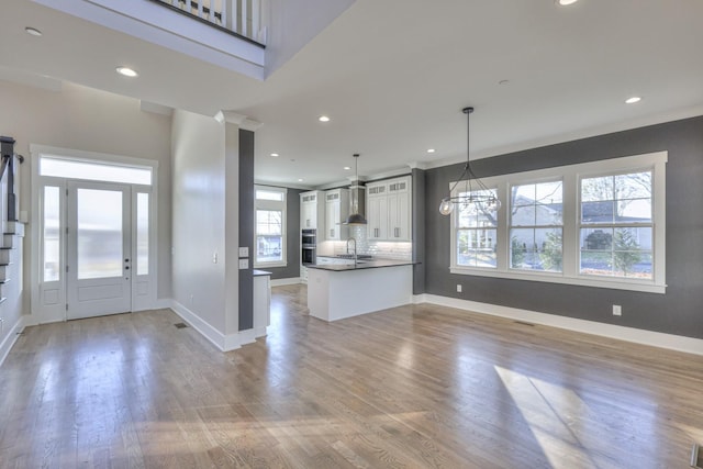 kitchen featuring wall chimney range hood, decorative light fixtures, a notable chandelier, light hardwood / wood-style floors, and white cabinetry