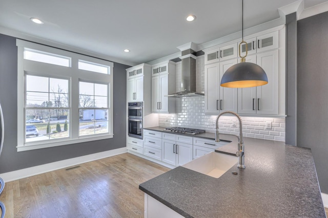 kitchen featuring wall chimney exhaust hood, stainless steel appliances, sink, pendant lighting, and white cabinetry