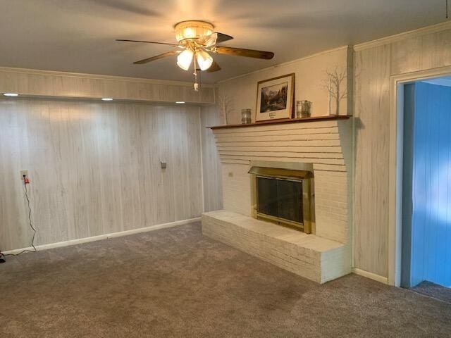 unfurnished living room featuring ceiling fan, wood walls, carpet floors, a fireplace, and ornamental molding