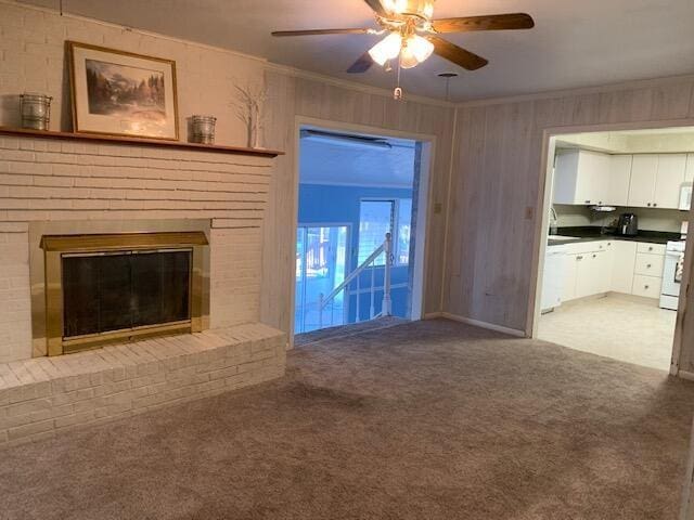 unfurnished living room with ceiling fan, wood walls, a fireplace, carpet, and ornamental molding