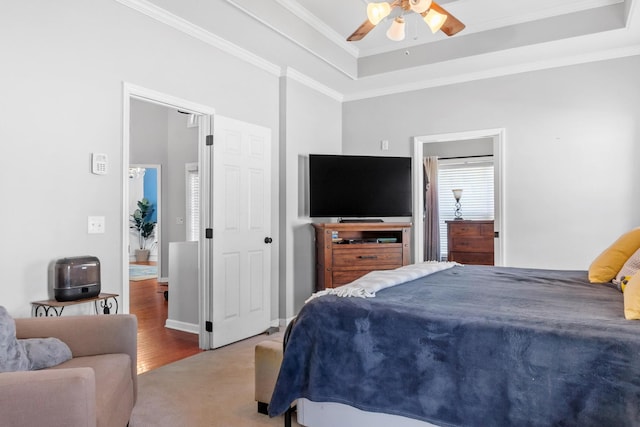 bedroom featuring a tray ceiling, ceiling fan, ornamental molding, and light colored carpet