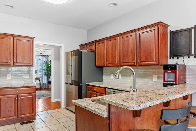 kitchen with a breakfast bar, tasteful backsplash, light tile patterned flooring, light stone counters, and kitchen peninsula