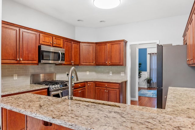 kitchen featuring light stone countertops, kitchen peninsula, backsplash, stainless steel appliances, and sink