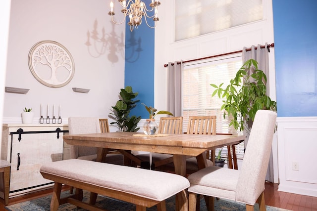 dining area with a decorative wall, wood finished floors, a notable chandelier, and wainscoting