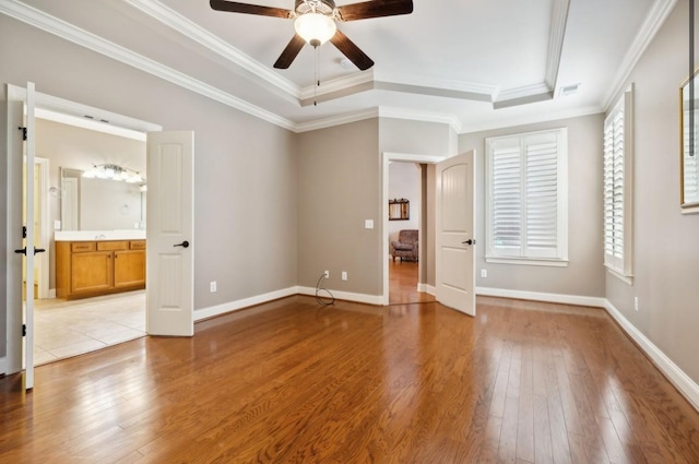 unfurnished bedroom featuring ensuite bathroom, a raised ceiling, ceiling fan, ornamental molding, and light hardwood / wood-style floors