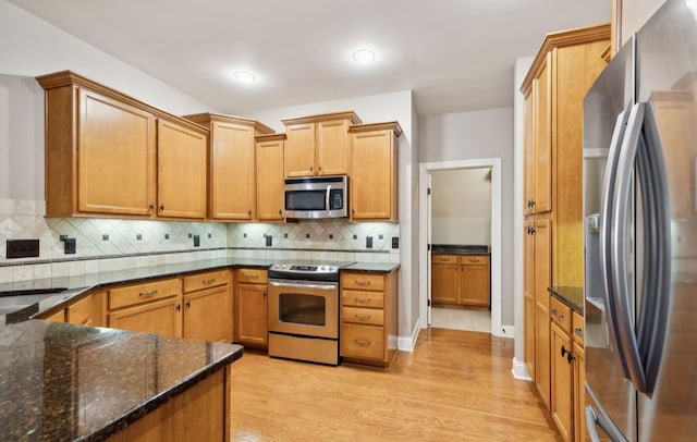 kitchen featuring decorative backsplash, light hardwood / wood-style flooring, appliances with stainless steel finishes, and dark stone counters