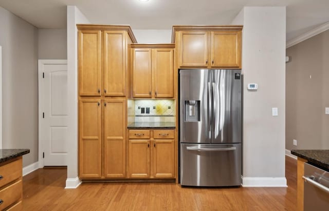 kitchen featuring decorative backsplash, dark stone countertops, light wood-type flooring, ornamental molding, and stainless steel appliances