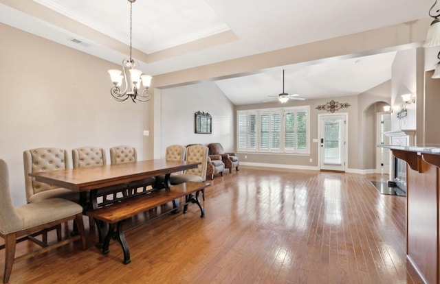 dining area featuring a tray ceiling, a fireplace, wood-type flooring, and ceiling fan with notable chandelier