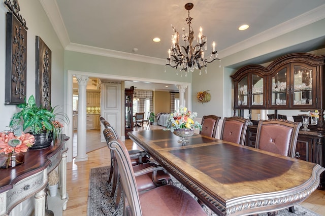 dining space featuring a notable chandelier, light hardwood / wood-style floors, ornamental molding, and decorative columns