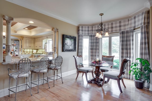 dining area featuring ornate columns, light hardwood / wood-style floors, a chandelier, and ornamental molding