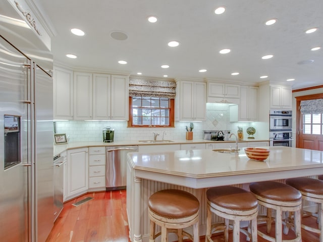 kitchen featuring a breakfast bar, a kitchen island with sink, sink, light hardwood / wood-style flooring, and stainless steel appliances