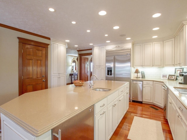 kitchen with sink, light hardwood / wood-style flooring, ornamental molding, an island with sink, and appliances with stainless steel finishes