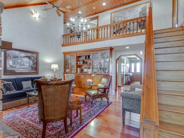 living room featuring light wood-type flooring, a towering ceiling, ceiling fan with notable chandelier, and wood ceiling