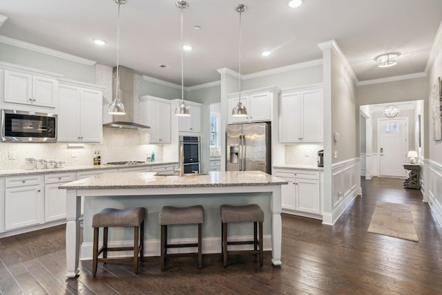 kitchen featuring white cabinetry, wall chimney exhaust hood, stainless steel appliances, an island with sink, and pendant lighting