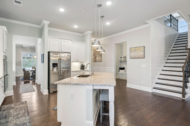 kitchen featuring stainless steel fridge, a kitchen island with sink, sink, pendant lighting, and white cabinetry