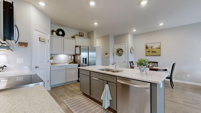 kitchen with a center island with sink, sink, light hardwood / wood-style flooring, decorative backsplash, and appliances with stainless steel finishes