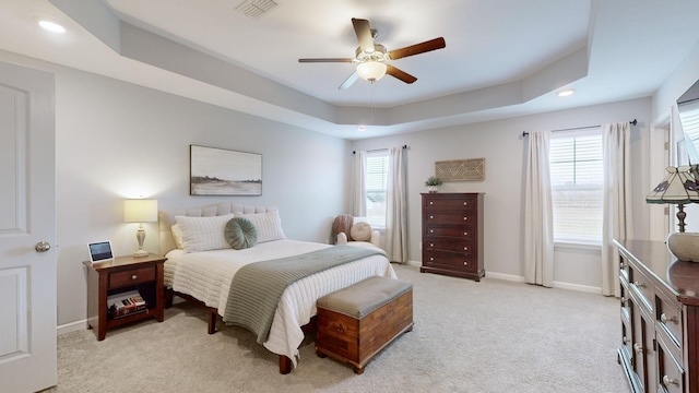 carpeted bedroom with ceiling fan and a raised ceiling