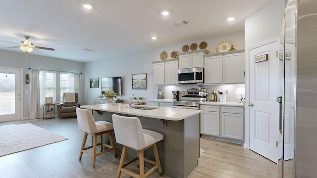 kitchen with sink, a kitchen breakfast bar, a kitchen island with sink, appliances with stainless steel finishes, and light wood-type flooring