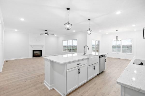 kitchen featuring white cabinetry, dishwasher, sink, hanging light fixtures, and an island with sink