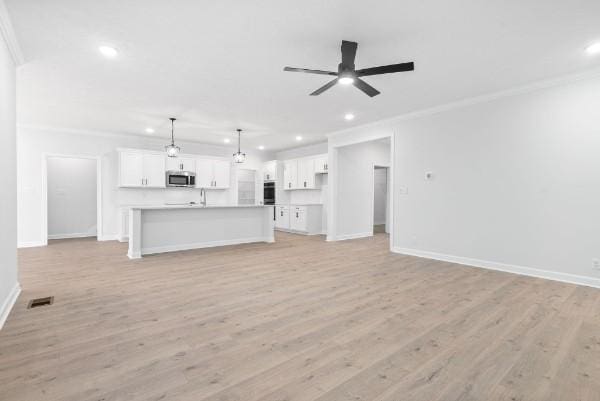 unfurnished living room featuring light wood-type flooring, ceiling fan, ornamental molding, and sink