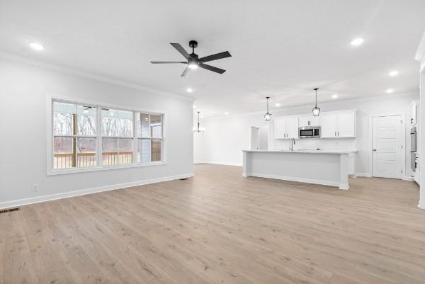 unfurnished living room featuring ceiling fan, sink, ornamental molding, and light wood-type flooring