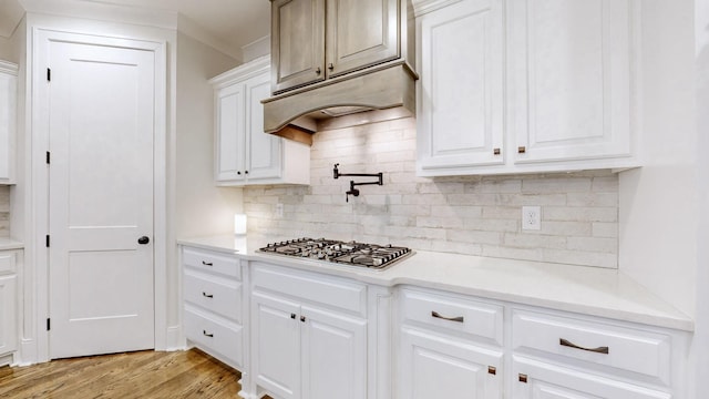 kitchen with stainless steel gas stovetop, decorative backsplash, light wood-type flooring, and white cabinetry