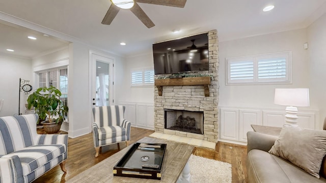 living room featuring a stone fireplace, ceiling fan, crown molding, and hardwood / wood-style flooring