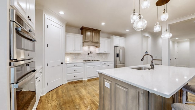 kitchen with appliances with stainless steel finishes, white cabinetry, a kitchen island with sink, and sink