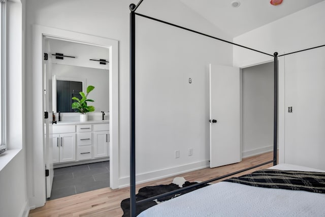 bedroom with ensuite bath, vaulted ceiling, sink, a barn door, and light hardwood / wood-style flooring