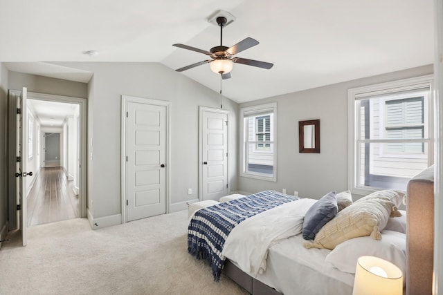 carpeted bedroom with multiple closets, ceiling fan, and vaulted ceiling