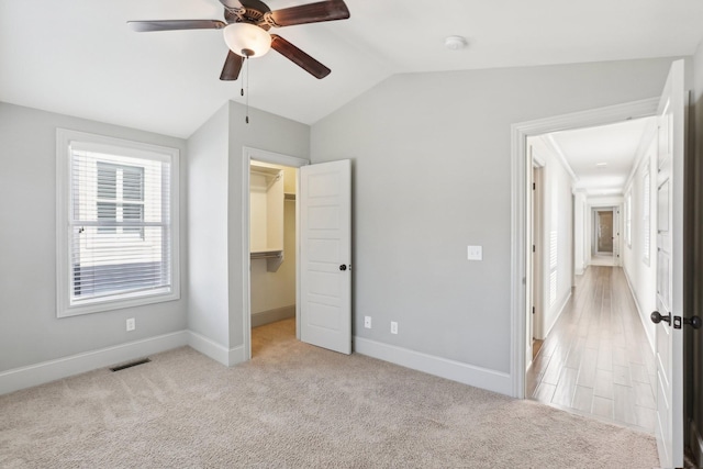 unfurnished bedroom with a walk in closet, ceiling fan, light colored carpet, and vaulted ceiling