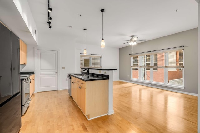 kitchen featuring light brown cabinetry, rail lighting, stainless steel appliances, sink, and hanging light fixtures