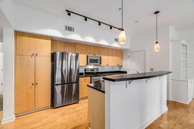 kitchen featuring appliances with stainless steel finishes, light wood-type flooring, a kitchen breakfast bar, decorative light fixtures, and a kitchen island