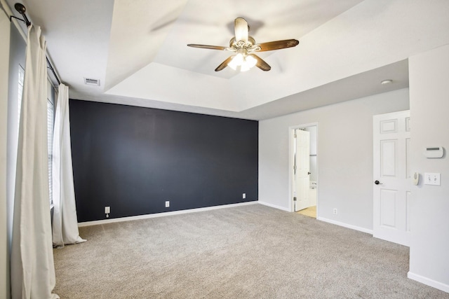 unfurnished bedroom with a tray ceiling, connected bathroom, ceiling fan, and light carpet