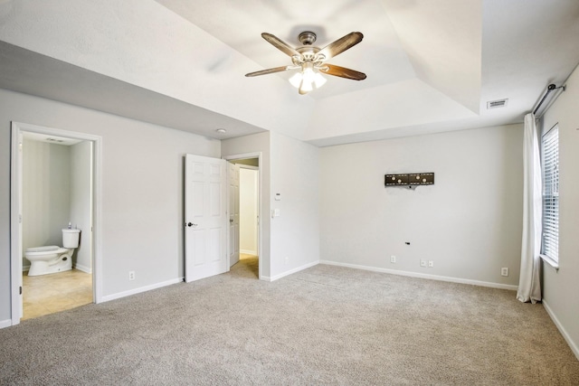 unfurnished bedroom featuring a tray ceiling, ceiling fan, light colored carpet, and ensuite bathroom