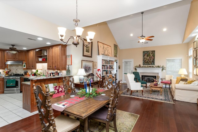 dining area with sink, high vaulted ceiling, ceiling fan with notable chandelier, and light wood-type flooring