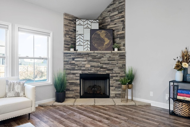 living room featuring a stone fireplace, wood-type flooring, and vaulted ceiling