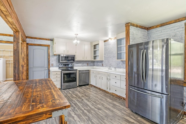 kitchen featuring hardwood / wood-style floors, white cabinets, decorative backsplash, appliances with stainless steel finishes, and brick wall