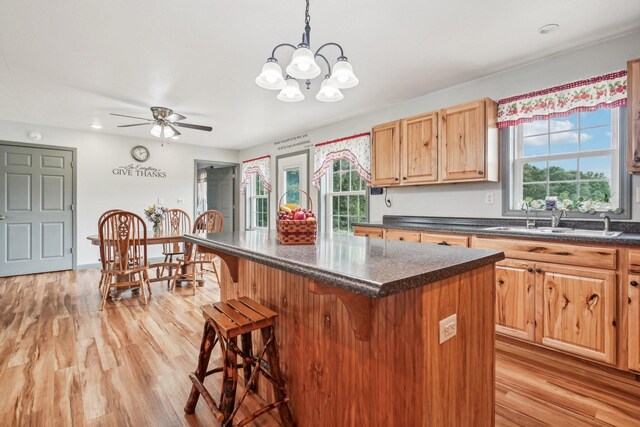 kitchen featuring pendant lighting, a breakfast bar, ceiling fan with notable chandelier, sink, and a kitchen island