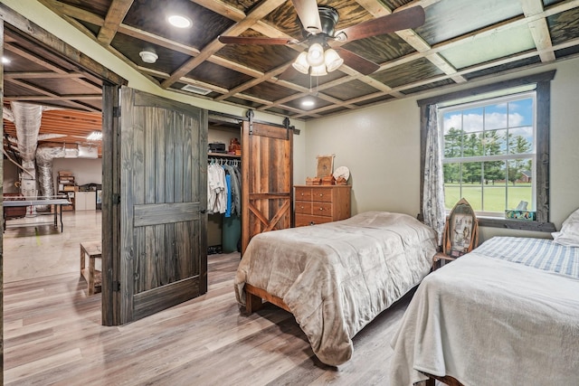 bedroom with ceiling fan, coffered ceiling, a barn door, a closet, and light wood-type flooring