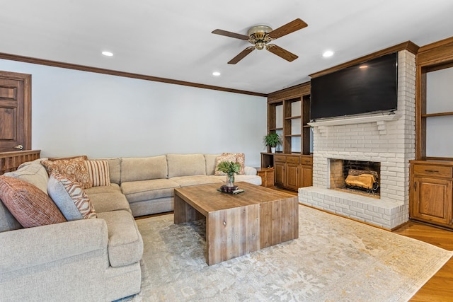 living room featuring a fireplace, ceiling fan, crown molding, and light hardwood / wood-style flooring