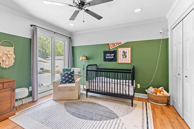 bedroom featuring a closet, a nursery area, crown molding, and ceiling fan