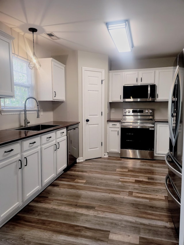 kitchen featuring appliances with stainless steel finishes, dark hardwood / wood-style flooring, sink, white cabinetry, and hanging light fixtures