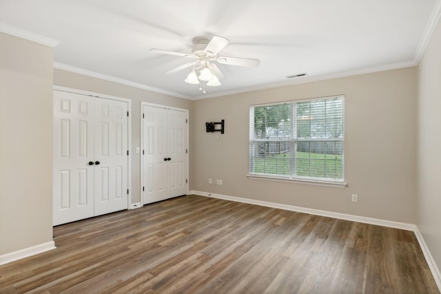 unfurnished bedroom featuring hardwood / wood-style floors, ceiling fan, crown molding, and two closets