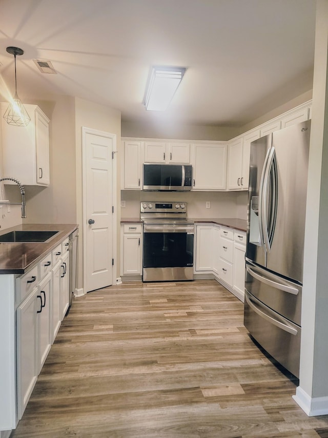 kitchen featuring sink, stainless steel appliances, pendant lighting, white cabinets, and light wood-type flooring