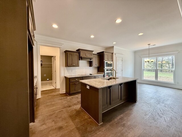 kitchen featuring light stone countertops, dark hardwood / wood-style flooring, backsplash, crown molding, and a center island with sink