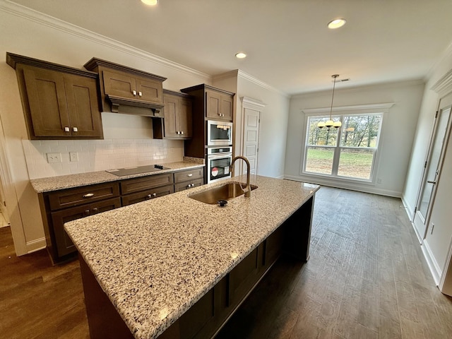 kitchen featuring light stone countertops, tasteful backsplash, stainless steel appliances, a kitchen island with sink, and sink