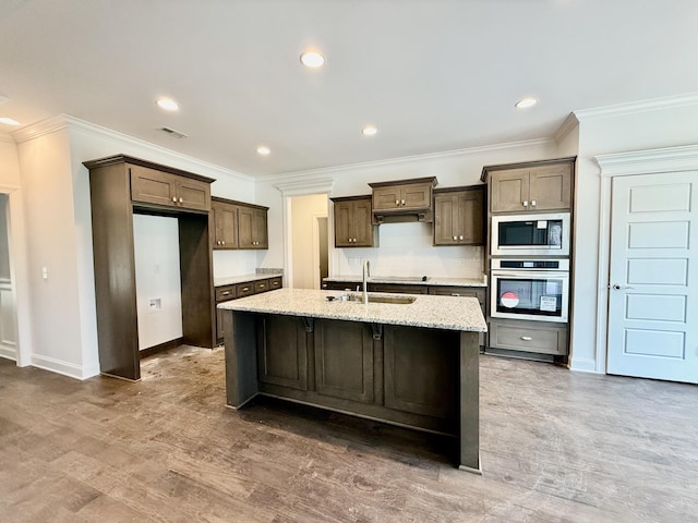 kitchen featuring stainless steel oven, a kitchen island with sink, sink, light stone countertops, and built in microwave